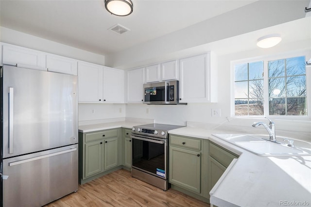 kitchen featuring appliances with stainless steel finishes, light hardwood / wood-style floors, green cabinets, and sink