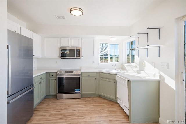 kitchen with green cabinets, sink, light wood-type flooring, and appliances with stainless steel finishes