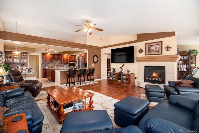 living room with a tiled fireplace, ceiling fan, lofted ceiling, and light wood-type flooring