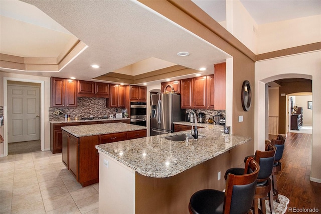 kitchen featuring a raised ceiling, light wood-type flooring, kitchen peninsula, and appliances with stainless steel finishes