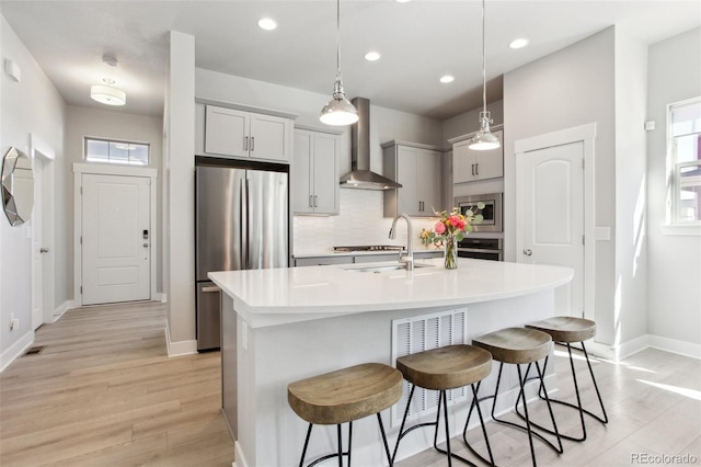 kitchen with wall chimney exhaust hood, light countertops, backsplash, appliances with stainless steel finishes, and a kitchen breakfast bar