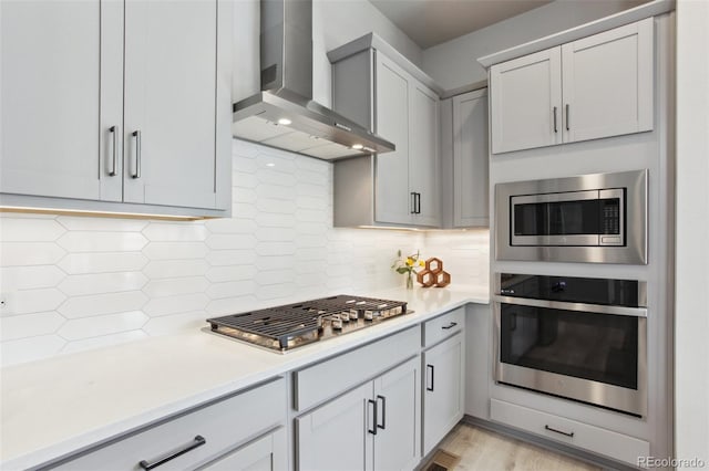 kitchen featuring wall chimney exhaust hood, appliances with stainless steel finishes, light countertops, and tasteful backsplash