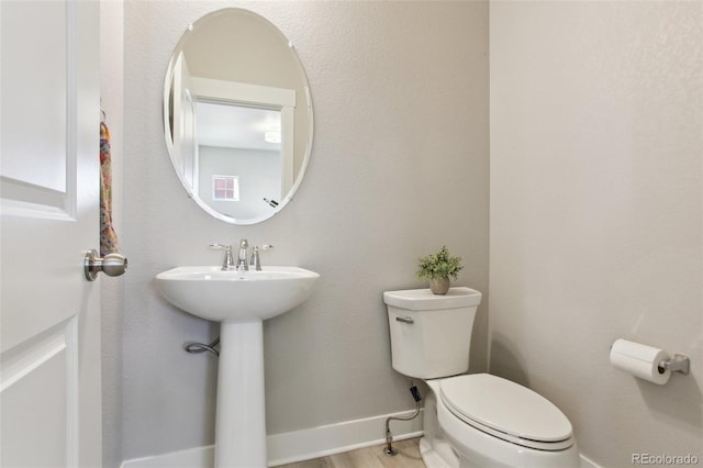 half bathroom featuring baseboards, toilet, and wood finished floors