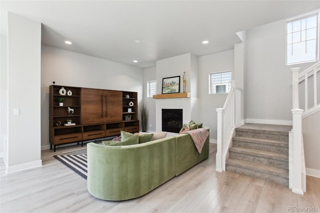 living room featuring light wood-type flooring, stairs, baseboards, and a fireplace