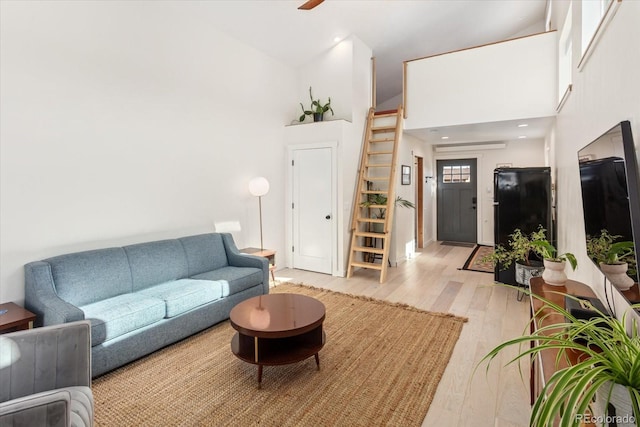 living room featuring ceiling fan, a towering ceiling, and light wood-type flooring