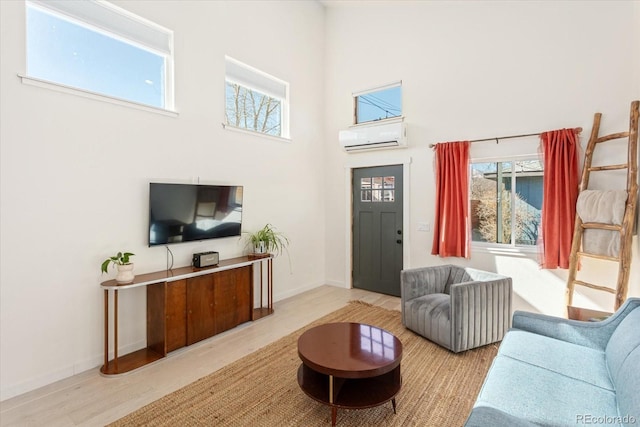 living room with light wood-type flooring, plenty of natural light, a wall unit AC, and a high ceiling