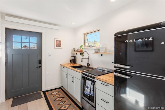 kitchen featuring stainless steel electric range oven, black refrigerator, sink, and wood counters