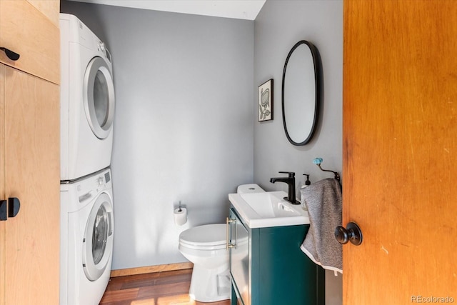 bathroom featuring stacked washer / dryer, wood-type flooring, vanity, and toilet