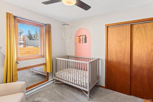 carpeted bedroom featuring ceiling fan, a baseboard radiator, a closet, and a crib