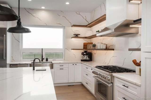 kitchen with light stone counters, premium appliances, wall chimney range hood, decorative light fixtures, and white cabinetry