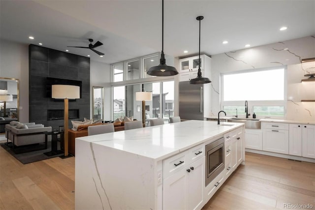 kitchen with a tile fireplace, a center island with sink, and white cabinetry