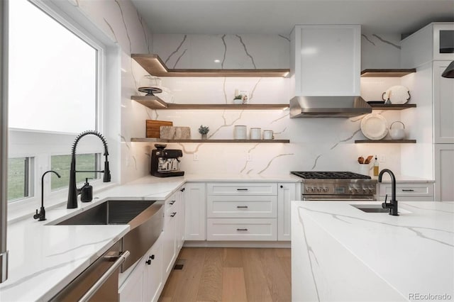 kitchen with light stone countertops, wall chimney exhaust hood, stainless steel range, light hardwood / wood-style flooring, and white cabinetry