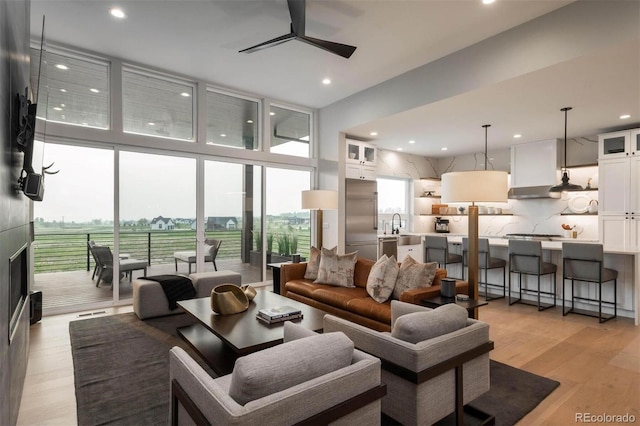 living room featuring ceiling fan, light wood-type flooring, a wall of windows, and sink