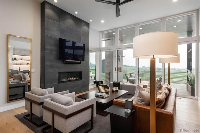 living room with a ceiling fan, wood finished floors, a high ceiling, a fireplace, and a wall of windows