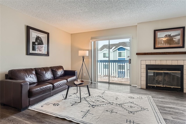 living area featuring a textured ceiling, wood finished floors, baseboards, and a tile fireplace