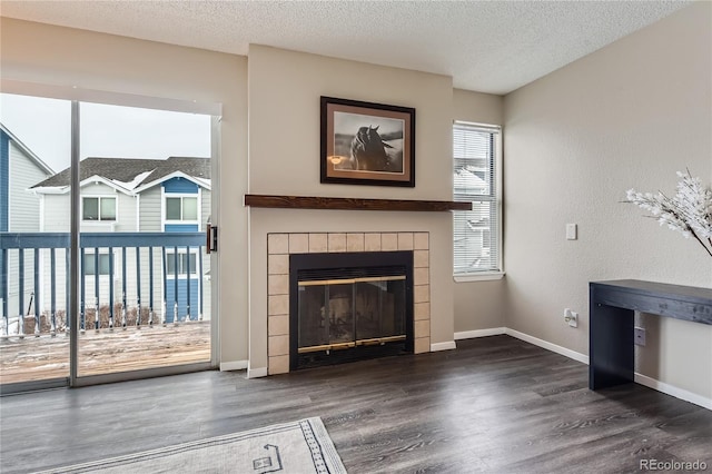 unfurnished living room with a tile fireplace, a textured ceiling, baseboards, and wood finished floors