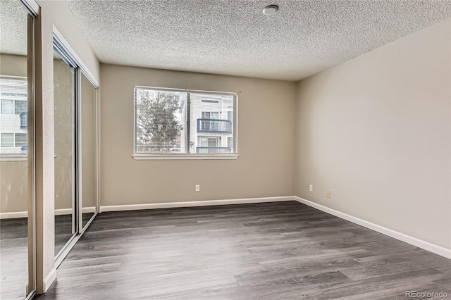 unfurnished bedroom with a textured ceiling, baseboards, and wood finished floors