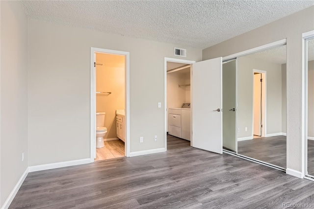 unfurnished bedroom featuring wood-type flooring, connected bathroom, a textured ceiling, and a closet