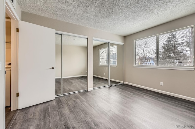 unfurnished bedroom with a textured ceiling, baseboards, multiple closets, and wood finished floors