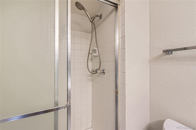 bathroom with toilet, a shower stall, and a textured wall