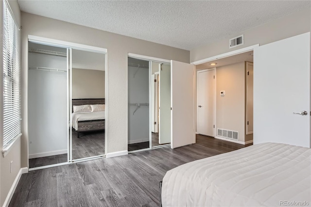 bedroom with wood finished floors, visible vents, two closets, and a textured ceiling