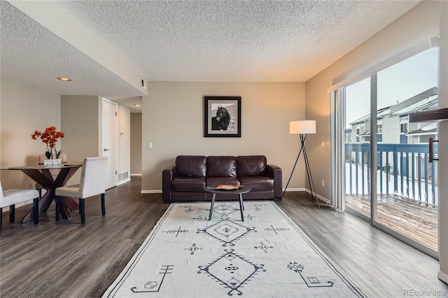 living area with visible vents, baseboards, a textured ceiling, and wood finished floors