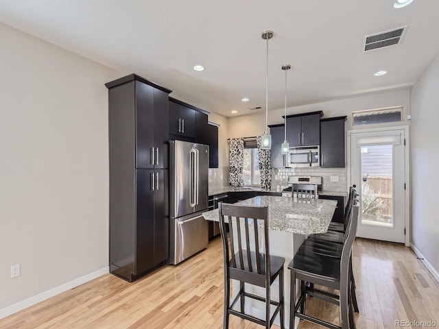 kitchen with decorative backsplash, stainless steel appliances, pendant lighting, a center island, and light hardwood / wood-style floors