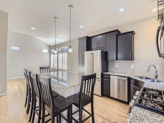 kitchen featuring sink, light wood-type flooring, appliances with stainless steel finishes, decorative light fixtures, and light stone counters