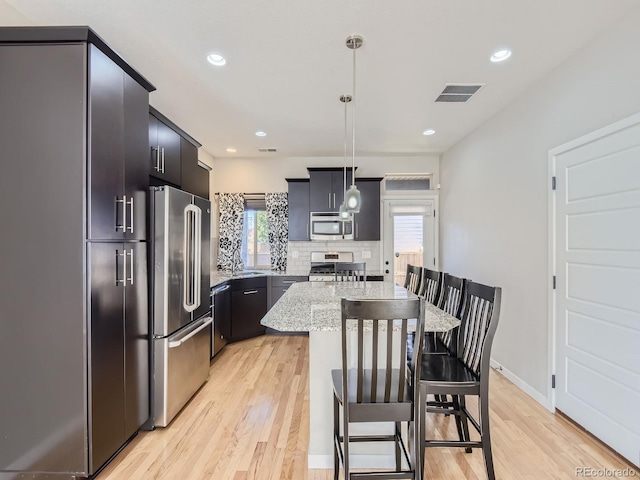 kitchen featuring a center island, light hardwood / wood-style floors, decorative light fixtures, a breakfast bar, and appliances with stainless steel finishes