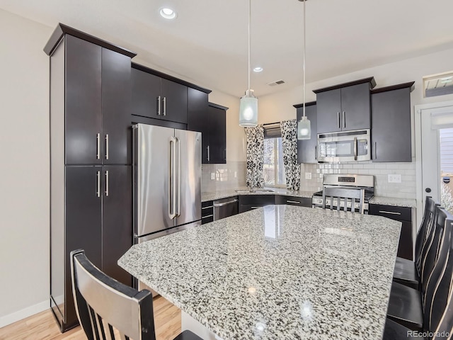 kitchen featuring decorative light fixtures, a center island, a kitchen bar, and appliances with stainless steel finishes