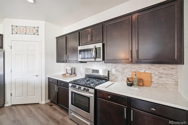 kitchen with light stone counters, stainless steel appliances, dark brown cabinets, and light wood-type flooring