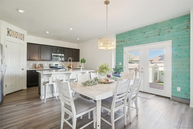 dining space with french doors, wood-type flooring, sink, and wood walls