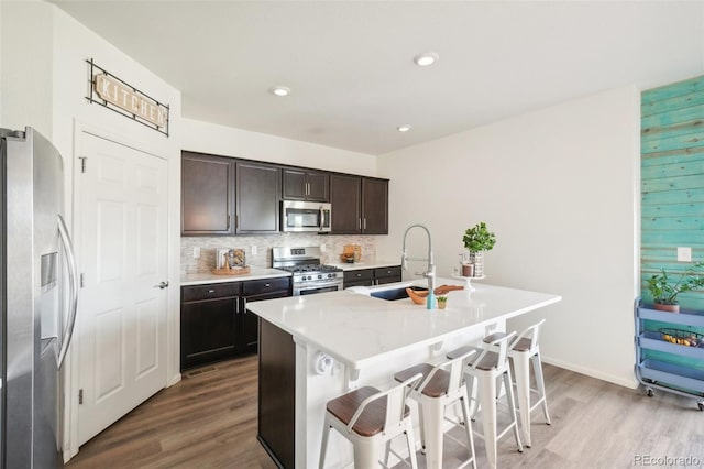 kitchen featuring appliances with stainless steel finishes, a kitchen island with sink, sink, and light wood-type flooring