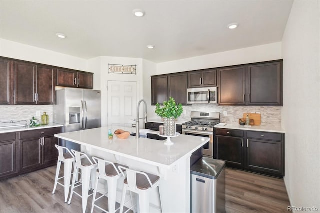 kitchen with stainless steel appliances, a breakfast bar area, dark brown cabinets, and a center island with sink