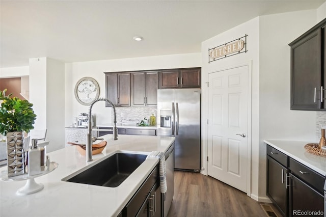 kitchen featuring sink, appliances with stainless steel finishes, dark brown cabinetry, dark hardwood / wood-style flooring, and decorative backsplash