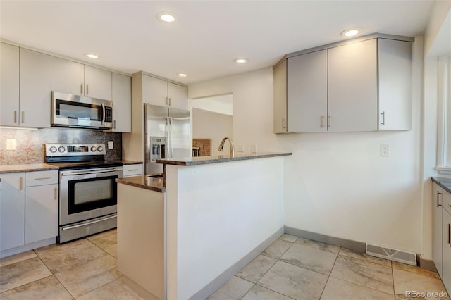 kitchen with decorative backsplash, kitchen peninsula, stainless steel appliances, and dark stone counters