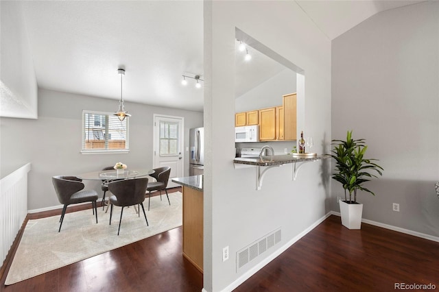 13906 Jackson St, Thornton, CO 80602 - kitchen with white microwave, lofted ceiling, dark wood-type flooring, stainless steel fridge, and a breakfast bar