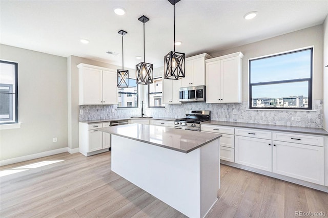 kitchen with a sink, white cabinets, light wood-style floors, appliances with stainless steel finishes, and tasteful backsplash