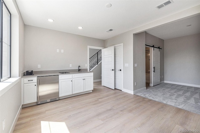 kitchen with light wood-type flooring, visible vents, built in fridge, white cabinetry, and a barn door