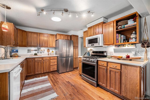 kitchen with light wood-type flooring, brown cabinets, a sink, stainless steel appliances, and light countertops
