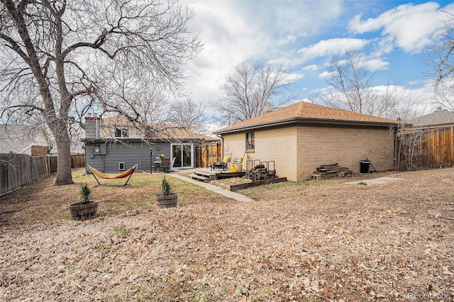 rear view of property featuring a wooden deck, brick siding, a fenced backyard, and a chimney