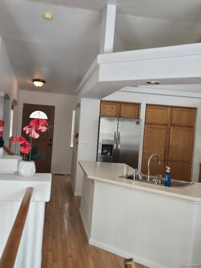 kitchen with stainless steel fridge with ice dispenser, sink, wood-type flooring, and a textured ceiling