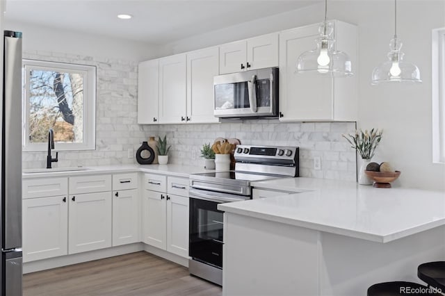 kitchen with stainless steel appliances, hanging light fixtures, sink, white cabinets, and tasteful backsplash