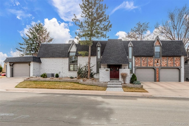 view of front facade with central air condition unit, a garage, driveway, and roof with shingles