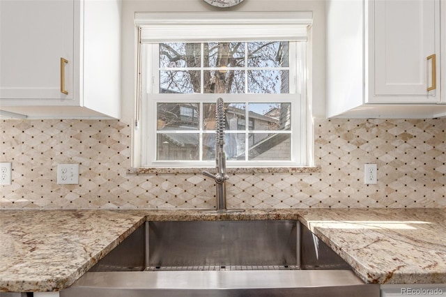 interior details with backsplash, white cabinets, light stone countertops, and a sink