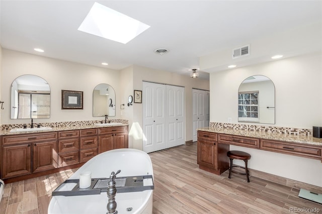 full bath featuring a sink, visible vents, a tub to relax in, and wood finished floors