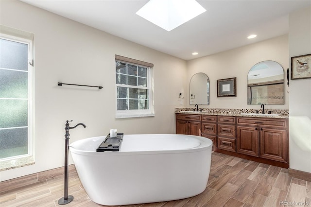 bathroom featuring wood tiled floor, double vanity, a skylight, a freestanding tub, and a sink