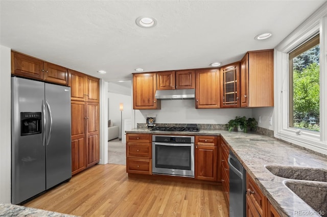 4398 Carter Trl, Boulder, CO 80301 - kitchen featuring stainless steel appliances, under cabinet range hood, light wood-style flooring, light stone countertops, and brown cabinetry