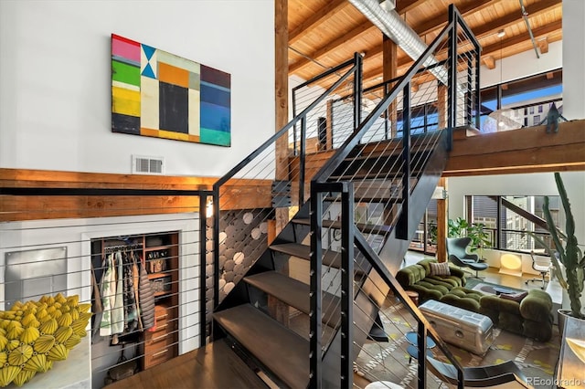 stairs featuring a high ceiling, hardwood / wood-style floors, wood ceiling, and beamed ceiling