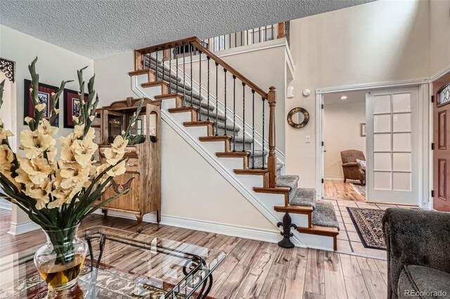 stairway with wood finished floors, baseboards, a towering ceiling, and a textured ceiling